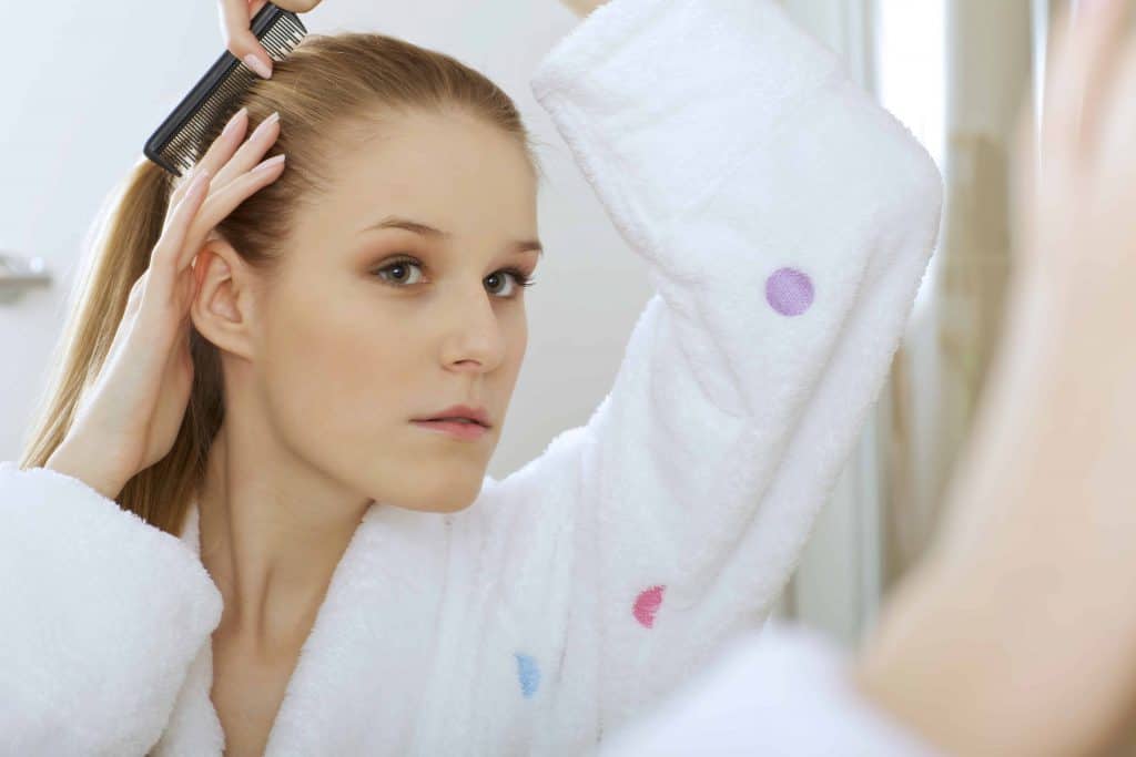  moteris šukuojasi plaukus prieš veidrodį